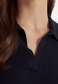 Námořnická pruhovaná blůzka s límečkem a designem do V, texturovaná látka a hladký povrch. Pohled zblízka na detaily výstřihu a límce.