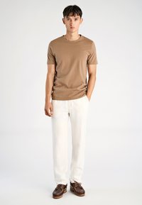 Korte mouwen tan t-shirt gemaakt van een gladde stof, gecombineerd met witte geribde broeken en bruine boten schoenen met veters en een gestructureerde zool.