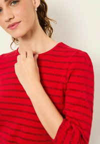 Rot gestreiftes Oberteil mit Glitzerakzenten, Rundhalsausschnitt und gerafften Ärmeln, das einen glatten Stoff und eine figurbetonte Silhouette präsentiert.
