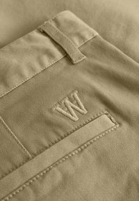 Pantalon en coton beige avec une poche arrière ornée d'un logo "W" brodé, tissu texturé et détail de couture plate.