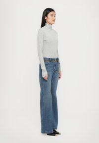 Gray turtleneck top paired with blue high-waisted flared jeans, featuring a gold chain belt, long sleeves, and pointed black shoes.