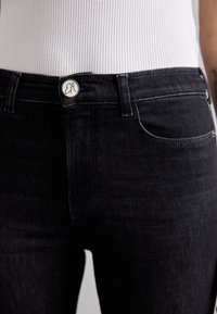 Jeans de mezclilla negra con una textura ligeramente descolorida, que cuentan con un cierre de botón plateado y un diseño tradicional de cinco bolsillos.