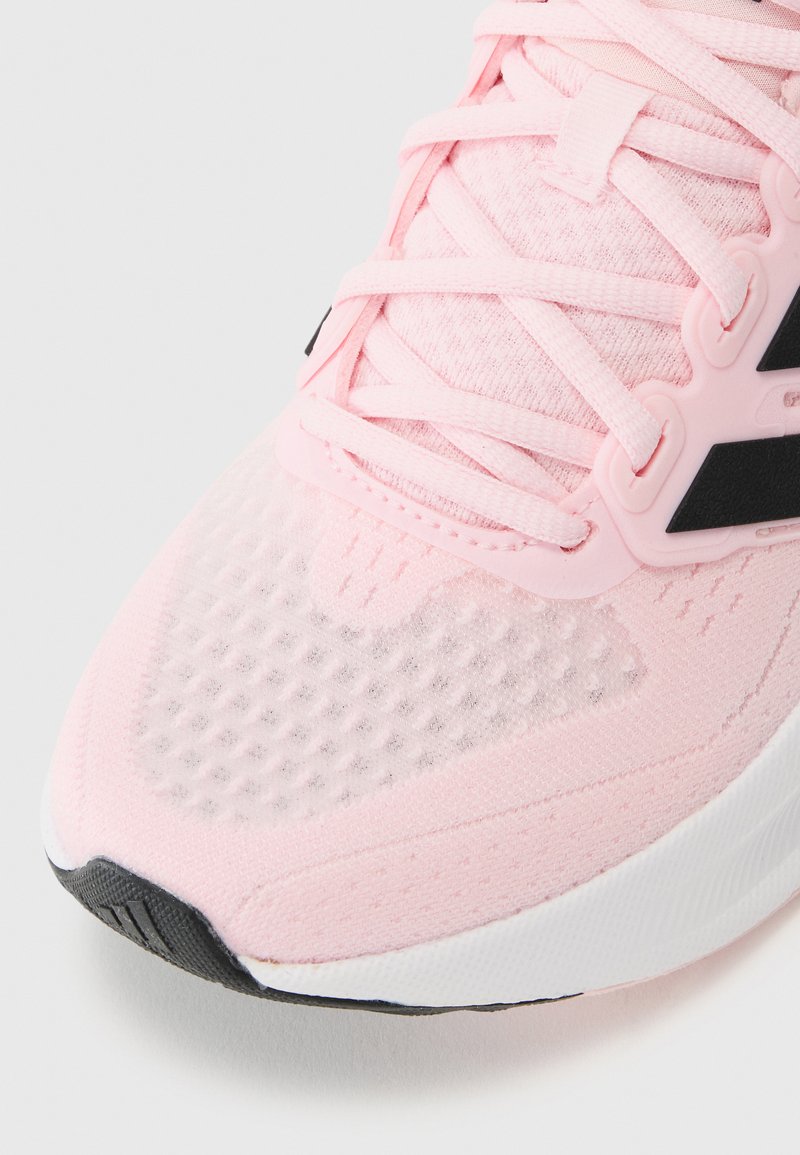 Scarpa atletica rosa con upper in rete testurizzata, lacci piatti e accenti neri. La suola è bianca con punta in gomma nera.