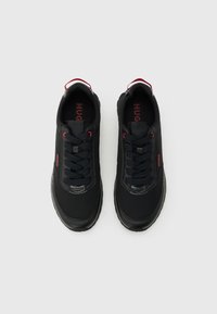 Μαύρα χαμηλά αθλητικά παπούτσια με κόκκινες λεπτομέρειες, μαύρα κορδόνια και το λογότυπο «HUGO» στο πλάι και στην εσωτερική σόλα, απεικονιζόμενα από πάνω σε γκρι φόντο.