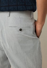 Pantalon rayé bleu clair et blanc, avec une poche arrière boutonnée et une coupe ajustée, confectionné dans un tissu léger.