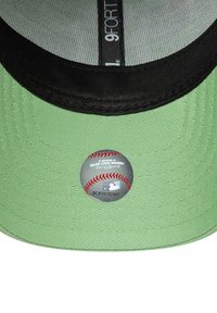 Casquette de baseball en tissu vert avec une visière noire. Présente un autocollant circulaire de la MLB à l'intérieur de la calotte, une surface texturée et un design structuré.