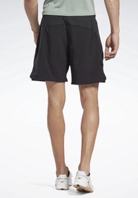 Svarta sportshorts med en avslappnad passform, med en mjuk textur och små sidofickor, ihopparade med vita sneakers.