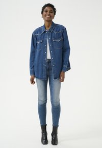 Gaiši zila denim jaka ar sudraba uzpērēm. Divas krūšu kabatas, nedaudz pārspīlēta piegriezuma. Valkāta ar šaurām biksēm un melniem potīšu zābakiem.