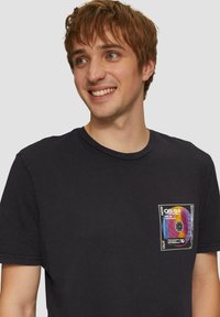 Zwarte katoenen t-shirt met korte mouwen en een ronde hals. Heeft een kleurrijke vinylplaat graphic op de linkerkant bij de borstzak.