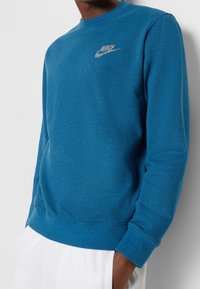 Felpa Nike blu con scollo rotondo, maniche lunghe, polsini e orlo ribattuti. Presenta un piccolo logo sul petto. Tessuto morbido.