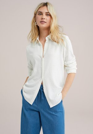 White button-up shirt with subtle textured pattern and long sleeves, paired with loose blue trousers. Light fabric, casual fit.