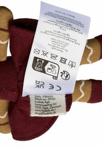 Juguete de felpa rojo y marrón con una cara sonriente, textura suave y etiqueta de cuidado adjunta. Las características son simples con un diseño caprichoso y costuras.