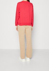 Czerwona bluza z okrągłym dekoltem, długimi rękawami i ściągaczami, zestawiona z beżowymi spodniami typu wide-leg oraz białymi trampkami.