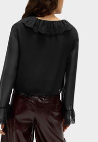 Czarna przezroczysta bluzka z falbaniastym koronkowym kołnierzykiem, długimi rękawami z koronkowymi mankietami, w połączeniu z wysokim stanem błyszczące bordo spodnie.