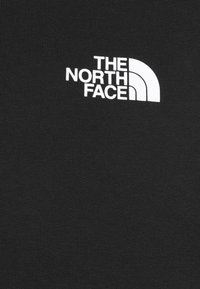 Logo blanc "The North Face" avec une forme de demi-dôme sur un tissu noir, centré dans la partie supérieure du vêtement.