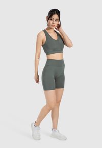Conjunto deportivo en verde apagado, compuesto por un sujetador deportivo ajustado y shorts de cintura alta, fabricados con una tela suave y elástica. Zapatillas blancas.