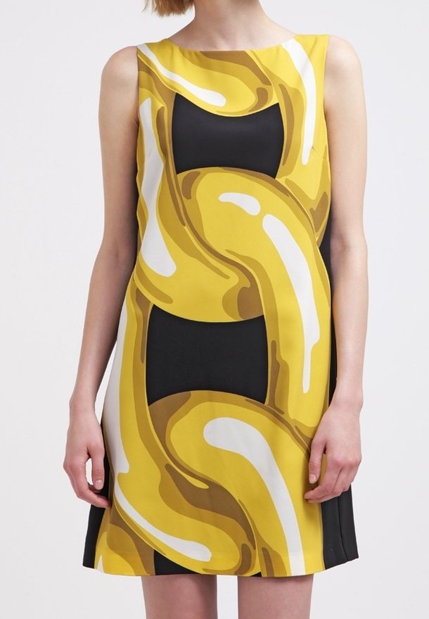 Robe noire sans manches avec un motif abstrait audacieux jaune et blanc en forme de maillons de chaîne à l'avant, portée par une personne debout.