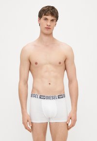 Valged puuvillased bokserid halli vöökohaga, millel on kirjas "DIESEL." Materjal tundub sile ja keha järgija, keskmise kõrgusega lõikega.
