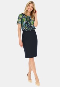 Bluzka w kwiatowy wzór w odcieniach niebieskiego, zielonego i białego z krótkim rękawem, zestawiona z dopasowaną granatową spódnicą ołówkową i beżowymi szpilkami.