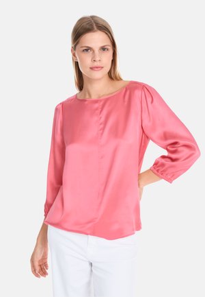 Rosa Satinbluse mit Dreiviertelärmeln, Rundhalsausschnitt und gerafften Manschetten. Trägt man mit weißen Hosen, die eine glatte, glänzende Textur zeigen.