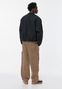 Crna bomber jakna s elastičnom gumom u struku, uparena s bež cargo hlačama koje imaju više džepova i opušteni kroj. Smeđe cipele.