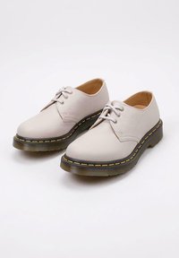 Scarpe stringate in pelle beige chiaro con finitura testurizzata, dotate di una suola nera spessa con cuciture gialle e un design classico della punta rotonda.
