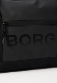 Svart nylonveske med teksturert overflate, som har en glidelåslomme og preget "BORG"-logo i matt finish.