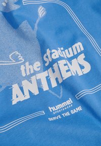 Blåt stof med hvid tekst "the stadium ANTHEMS", hummel sportswear-logo og sloganet "SERVE THE GAME", med delvist grafisk design.