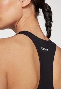 Mustmust musterniga tank top, millel on ümmargune seljaosa disain, DKNY valge logo ülemisel seljal, sile tekstuur ja tihe siluett.