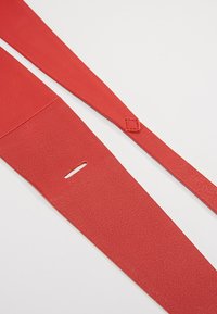 Cinghie in pelle rossa con una finitura testurizzata, dotate di una fessura e di un accento quadrato vicino all'estremità. Forma piatta ed allungata per una chiusura sicura.
