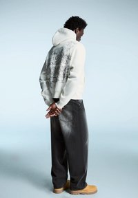 Felpa grigia chiara con grafica sul retro, abbinata a pantaloni larghi grigi scuri e scarpe chunky color sabbia. Tessuto morbido, stile casual.