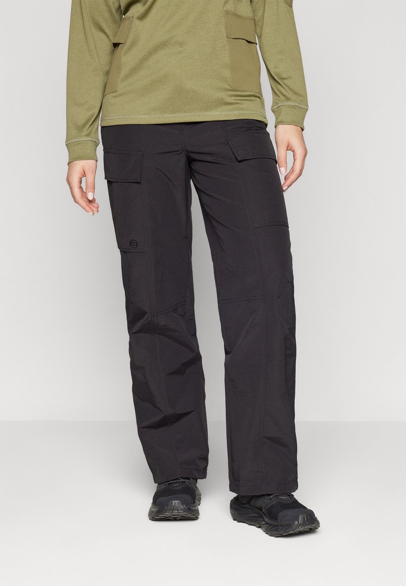 Black cargo pants feature multiple pockets, a relaxed fit, and durable fabric. Paired with a green long-sleeve top and black shoes.