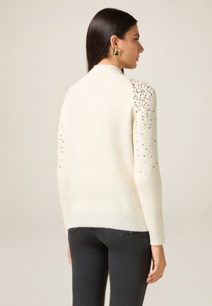 Cream-colored sweater with ribbed texture and sequin embellishments on the shoulders. Features long sleeves and a relaxed fit.