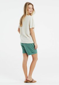 Camiseta de manga corta beige combinada con pantalones cortos verdes. La camiseta tiene un corte relajado; los pantalones cortos tienen bolsillos laterales y dobladillos enrollados.
