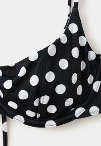 Haut de bikini noir avec de grands pois blancs et fines bretelles, montrant les détails des coutures sur le tissu.