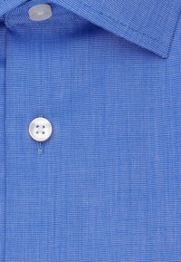 Niebieska koszula z długim rękawem o teksturowanym, subtelnym prążkowanym wzorze. Posiada klasyczny kołnierzyk i jeden biały guzik przy szyi.