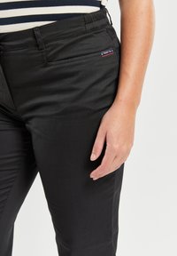 Pantalones negros ajustados con una textura suave, que cuentan con un bolsillo lateral y una pequeña etiqueta con acentos rojos y azules en la cinturilla.
