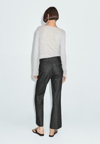 Maglia grigia a maniche lunghe realizzata in un materiale testurizzato, abbinata a pantaloni larghi scuri. Cuciture visibili sulle tasche, semplici sandali.