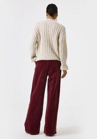 Crème kabeltrui met ribbeltextuur en een ronde hals, gecombineerd met hoogwaisted burgundy ribfluwelen broek met wijde pijpen.