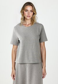 Korte mouw, ronde hals top in een gestructureerde stof met een geometrisch patroon in beige, blauw en bruin. Relaxed fit met een gebogen zoom.