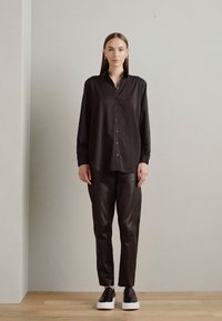 Black button-up shirt with long sleeves and a collar, paired with fitted black leather pants and sleek black sneakers with white soles.