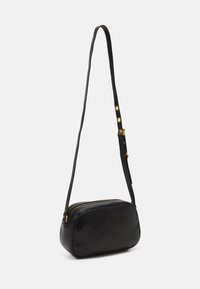 Borsa a tracolla nera in pelle con texture liscia, forma ovale, dettagli in metallo dorato e una tracolla sottile e regolabile. Chiusura con zip nella parte superiore.