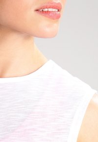 Close-up of a woman's neck and shoulder, displaying a white, sheer fabric top with a soft texture and minimal seam detailing.