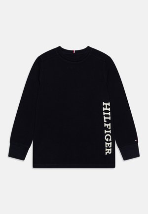 Czarna koszulka z długim rękawem i okrągłym dekoltem z pionowym, białym napisem „HILFIGER” po prawej stronie oraz małym logo na lewym mankiecie.