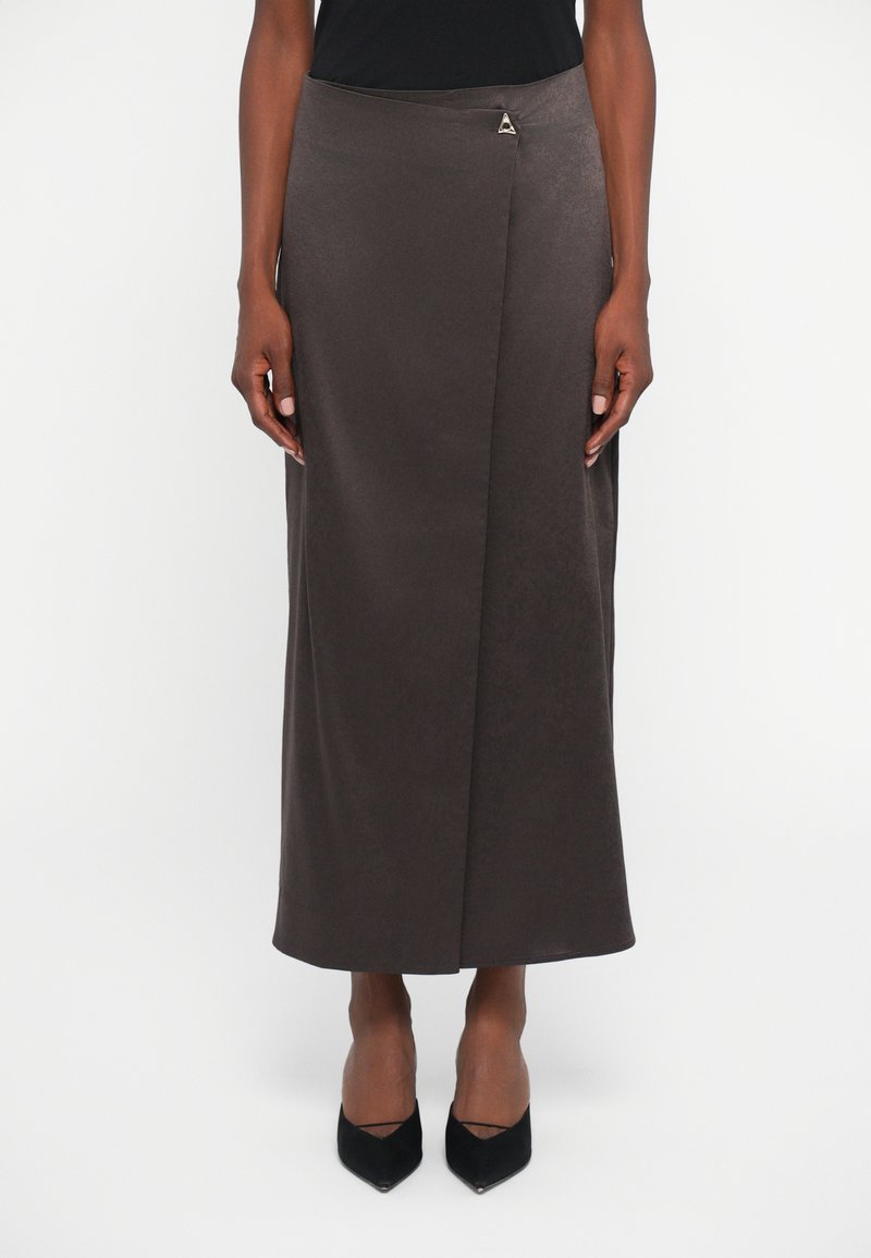 Falda midi de estilo envolvente en marrón oscuro con un cierre triangular plateado, combinada con unos tacones negros de punta y una blusa negra.