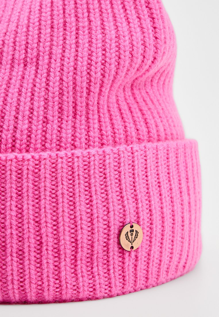 Różowa dzianinowa czapka wykonana z miękkiej przędzy, z ribbowanym wzorem i małą drewnianą metką z kwiatowym wzorem na mankiecie.