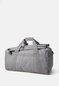 Sac de sport gris fabriqué en tissu durable, avec deux poignées supérieures, une bandoulière ajustable et des poches extérieures pour un rangement supplémentaire.