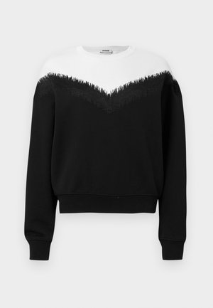 Sweatshirt preta com a parte superior branca e detalhe em franjas pretas. Punhos e bainha canelados, criando uma silhueta justa.