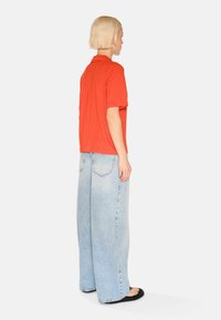 Rød kortærmet polo-shirt parret med lyseblå bredbenede jeans. Jeansene har baglommer og en lysnet vask. Sorte sandaler fuldender looket.