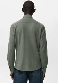 Camisa verde de manga larga con tejido texturizado, puños abotonados y cuello, con un corte recto y detalle en el yugo trasero.